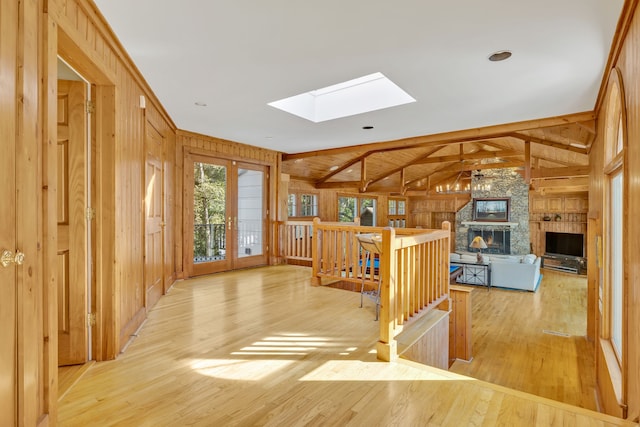 kitchen featuring vaulted ceiling with skylight, wooden walls, a stone fireplace, and light wood-type flooring