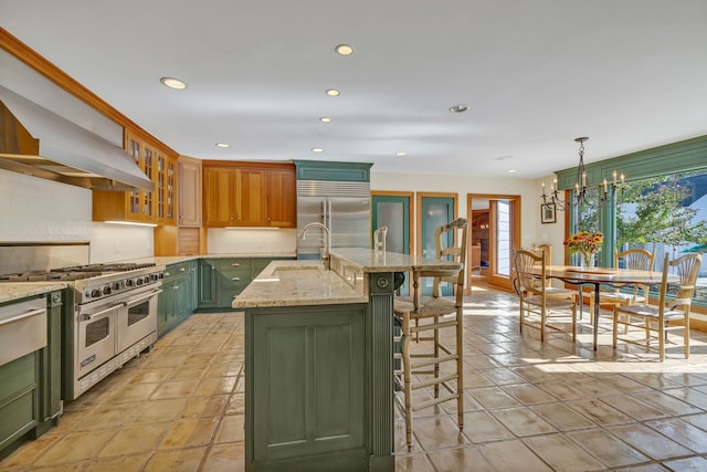 kitchen featuring decorative light fixtures, high quality appliances, an island with sink, a notable chandelier, and light stone countertops