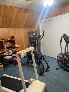 exercise room with carpet flooring, lofted ceiling, wood walls, and ceiling fan