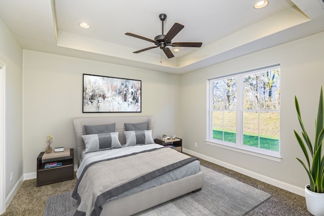 carpeted bedroom featuring ceiling fan and a tray ceiling