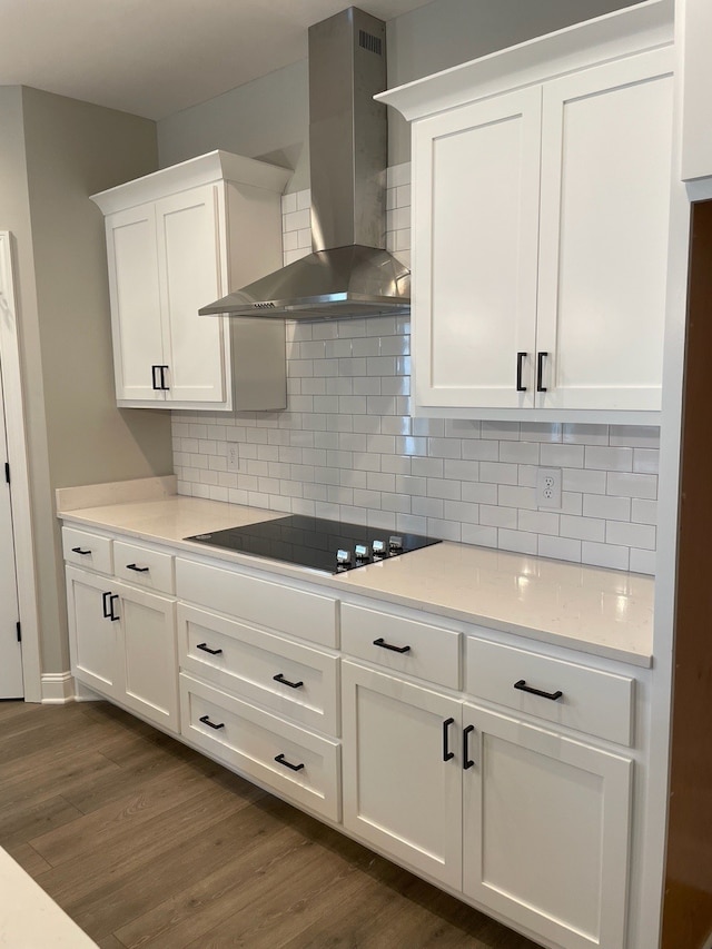 kitchen featuring tasteful backsplash, dark wood-type flooring, black electric cooktop, wall chimney exhaust hood, and white cabinets