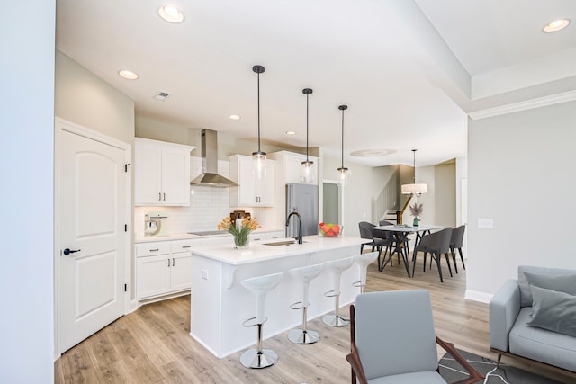 kitchen featuring light hardwood / wood-style floors, pendant lighting, stainless steel fridge, wall chimney range hood, and a kitchen breakfast bar