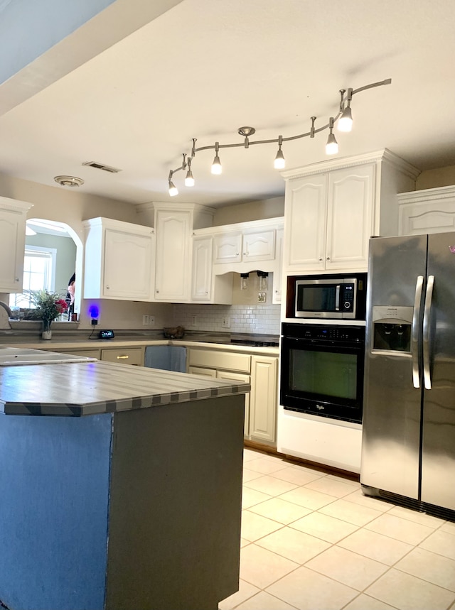 kitchen with appliances with stainless steel finishes, tasteful backsplash, sink, light tile patterned floors, and white cabinetry