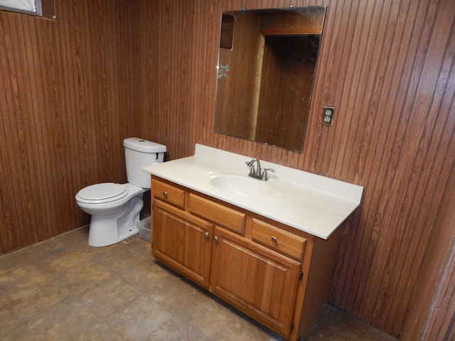 bathroom featuring wood walls, vanity, concrete floors, and toilet