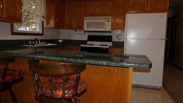 kitchen with white appliances, a breakfast bar, sink, and light tile floors