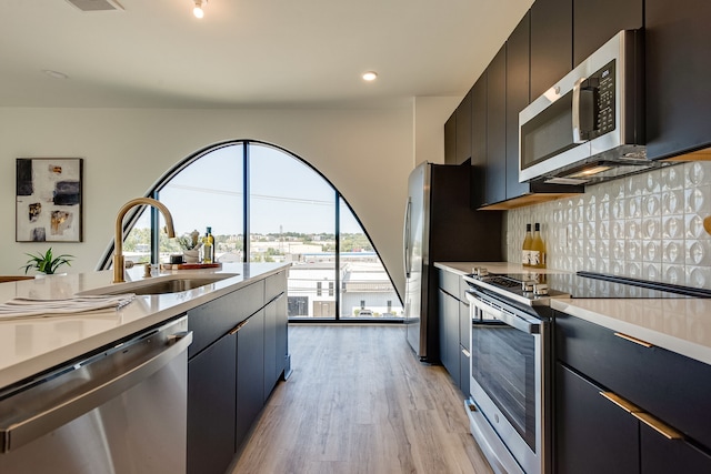 kitchen with appliances with stainless steel finishes, sink, tasteful backsplash, and light hardwood / wood-style floors