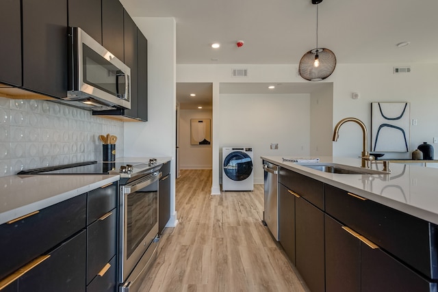 kitchen with stainless steel appliances, washer / dryer, backsplash, light wood-type flooring, and sink