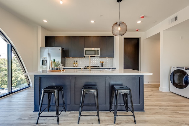 kitchen featuring appliances with stainless steel finishes, light hardwood / wood-style flooring, washer / clothes dryer, and a center island with sink