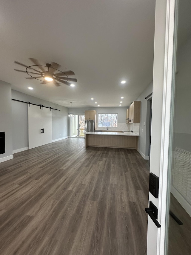 unfurnished living room featuring dark wood-type flooring, a barn door, and ceiling fan