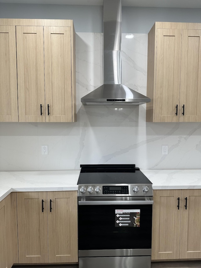 kitchen featuring wall chimney exhaust hood, light brown cabinetry, light stone counters, stainless steel electric stove, and backsplash