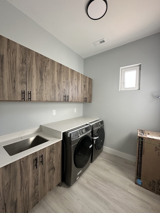 washroom with sink, washing machine and dryer, cabinets, and light wood-type flooring