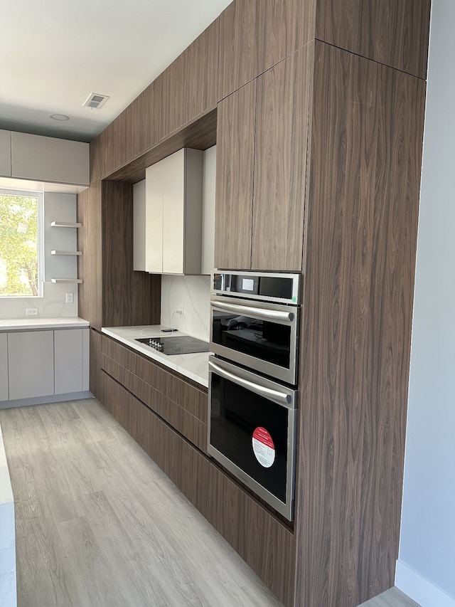 kitchen with black electric cooktop, double oven, and light wood-type flooring