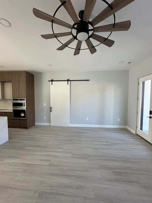 unfurnished living room featuring light hardwood / wood-style floors, a barn door, and ceiling fan