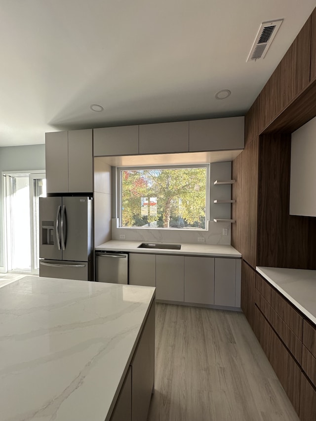 kitchen featuring stainless steel appliances, sink, light stone counters, and light hardwood / wood-style floors