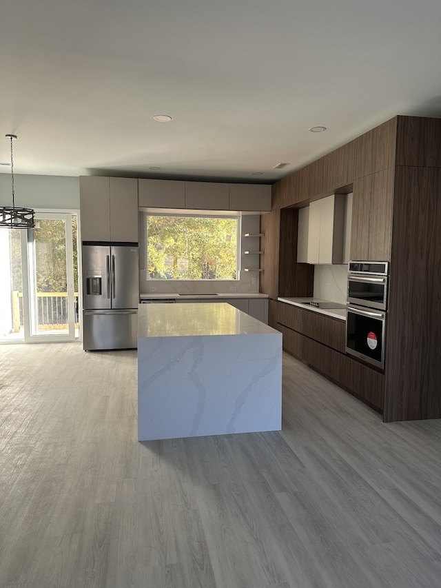 kitchen featuring decorative light fixtures, a chandelier, light hardwood / wood-style flooring, appliances with stainless steel finishes, and light stone countertops