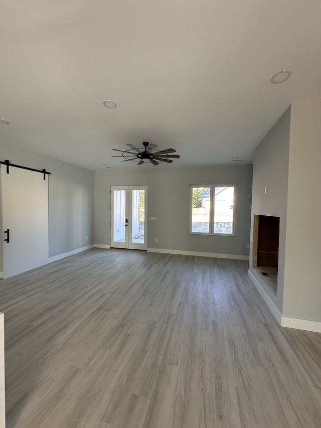 unfurnished living room featuring light hardwood / wood-style floors, a barn door, and ceiling fan