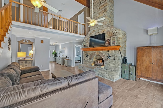 living room with a stone fireplace, high vaulted ceiling, beamed ceiling, ornamental molding, and ceiling fan