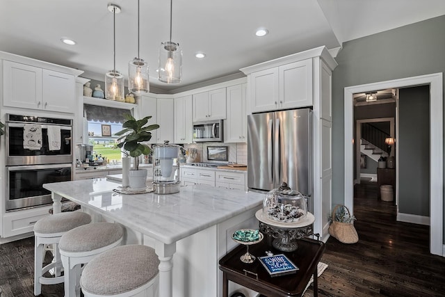 kitchen with appliances with stainless steel finishes, a center island, hanging light fixtures, and white cabinets