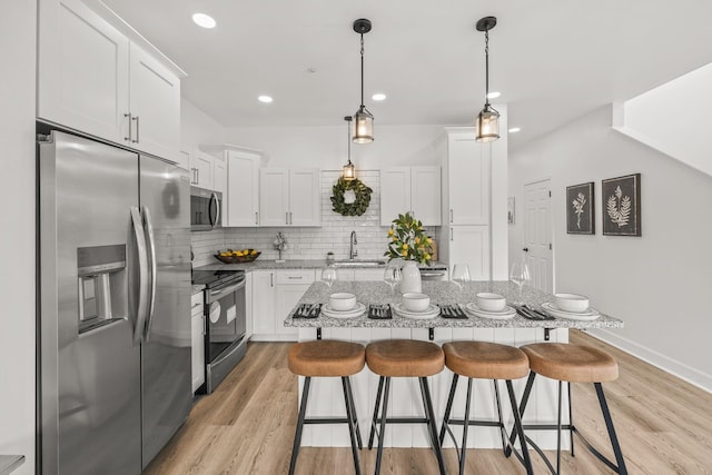 kitchen with appliances with stainless steel finishes, a breakfast bar, light hardwood / wood-style flooring, white cabinets, and a kitchen island