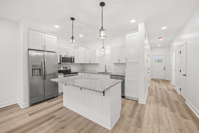 kitchen featuring white cabinets, hanging light fixtures, light wood-type flooring, a kitchen island, and stainless steel appliances