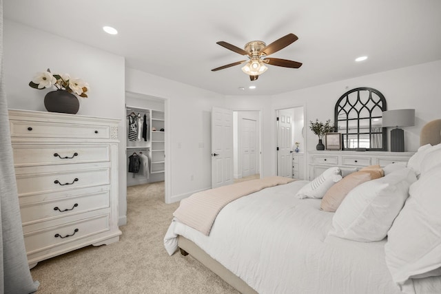 carpeted bedroom with a walk in closet, a closet, ensuite bath, and ceiling fan