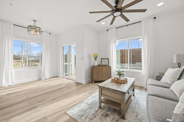 living room featuring ceiling fan with notable chandelier, light wood-type flooring, and plenty of natural light