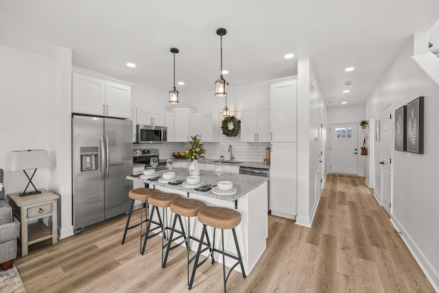 kitchen with hanging light fixtures, white cabinetry, light hardwood / wood-style flooring, and stainless steel appliances