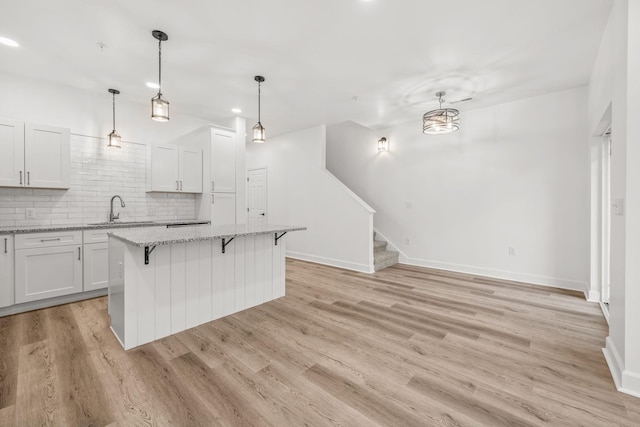 kitchen featuring tasteful backsplash, light stone counters, white cabinets, light hardwood / wood-style floors, and a kitchen island