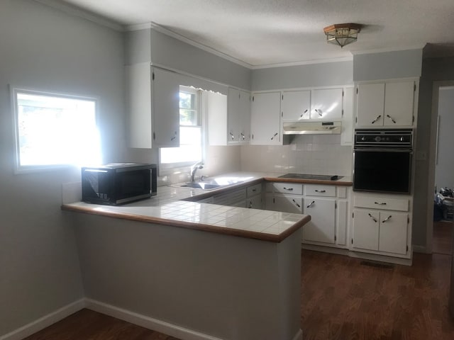 kitchen with sink, kitchen peninsula, dark wood-type flooring, white cabinetry, and black appliances