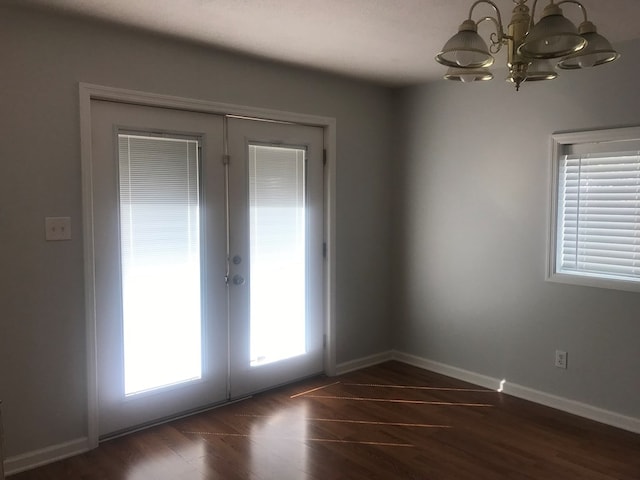 empty room with a healthy amount of sunlight, dark hardwood / wood-style flooring, french doors, and a notable chandelier