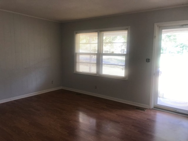 spare room featuring a healthy amount of sunlight, ornamental molding, and dark wood-type flooring