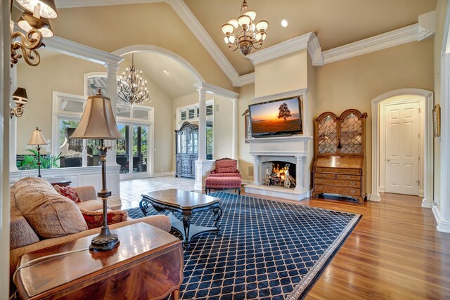 living area with a notable chandelier, wood finished floors, a lit fireplace, ornamental molding, and decorative columns