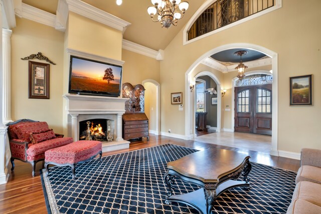 living area with arched walkways, ornamental molding, wood finished floors, an inviting chandelier, and a lit fireplace