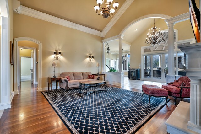 living room featuring arched walkways, decorative columns, wood-type flooring, ornamental molding, and a chandelier