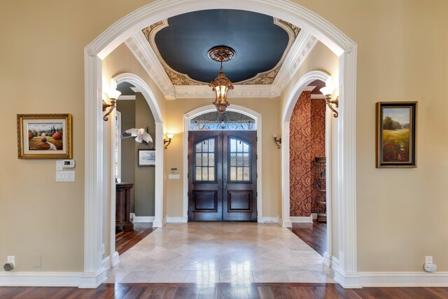 foyer entrance with arched walkways, french doors, ornamental molding, and baseboards