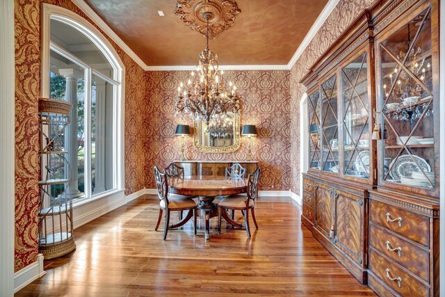 dining room featuring wood finished floors, crown molding, baseboards, and wallpapered walls