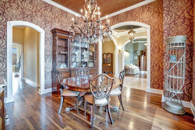 dining area with wallpapered walls, baseboards, arched walkways, wood finished floors, and crown molding