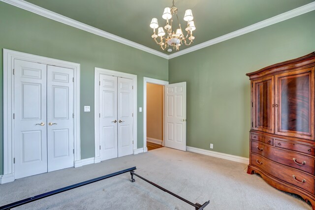 unfurnished bedroom featuring carpet floors, baseboards, multiple closets, ornamental molding, and an inviting chandelier