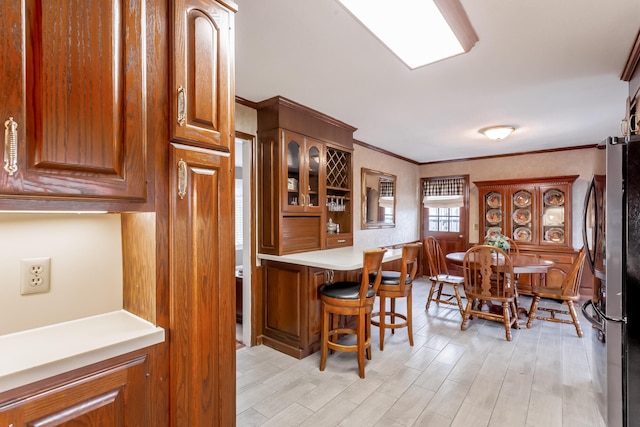 kitchen featuring crown molding, a breakfast bar, light hardwood / wood-style floors, kitchen peninsula, and stainless steel refrigerator