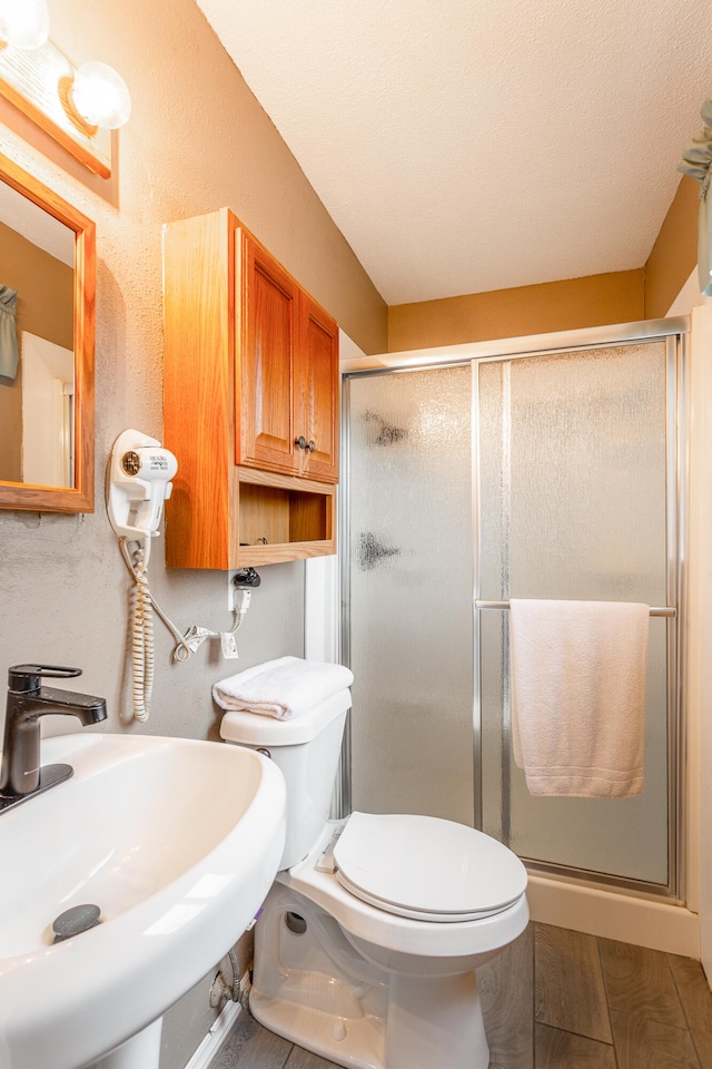 bathroom featuring a shower with shower door, sink, and toilet