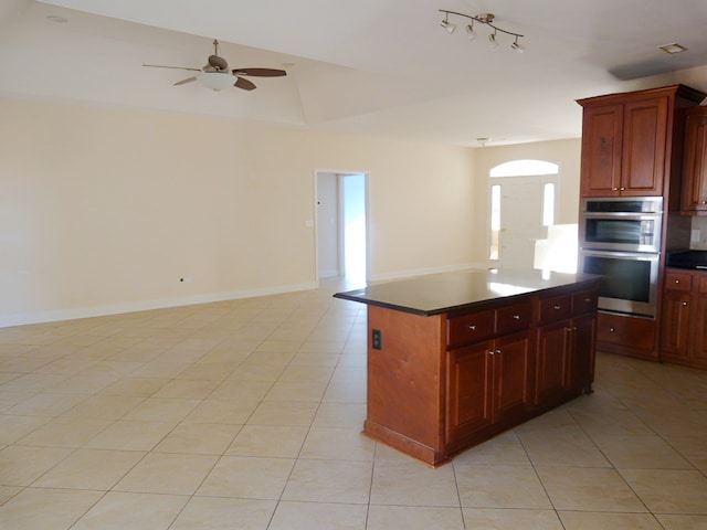 kitchen featuring ceiling fan, stainless steel double oven, a kitchen island, and light tile flooring