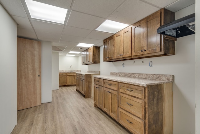 kitchen featuring wall chimney range hood, light hardwood / wood-style floors, a drop ceiling, and sink