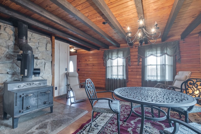 dining space with an inviting chandelier, a wood stove, and beam ceiling