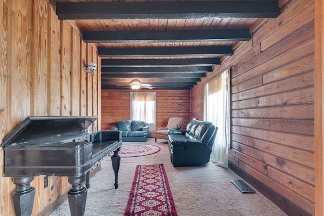 interior space featuring ceiling fan, wooden walls, beam ceiling, wood ceiling, and light carpet