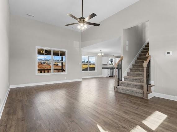 unfurnished living room with ceiling fan with notable chandelier, dark wood-type flooring, and a high ceiling