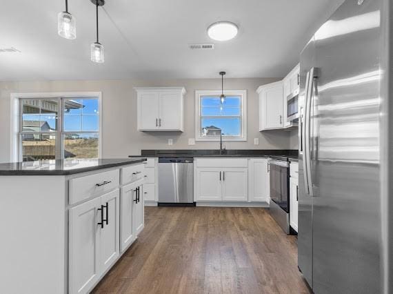 kitchen with white cabinets, hanging light fixtures, appliances with stainless steel finishes, and dark hardwood / wood-style flooring