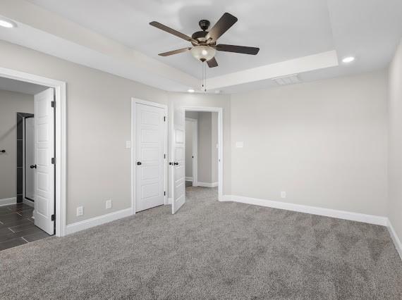 unfurnished bedroom with ceiling fan, dark carpet, and a tray ceiling