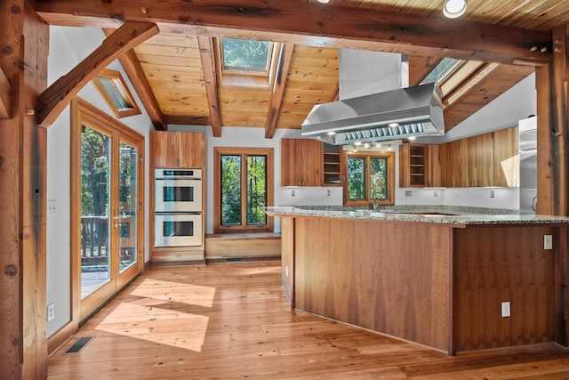 kitchen with island range hood, stone counters, vaulted ceiling with skylight, and light hardwood / wood-style flooring