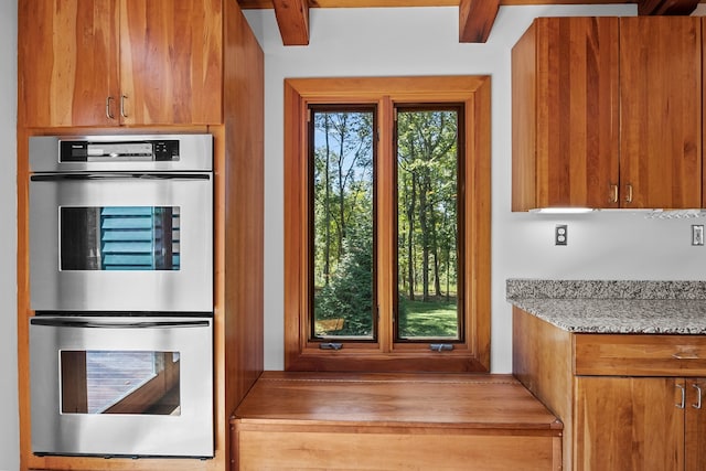 kitchen featuring beamed ceiling, light stone counters, double oven, and wood-type flooring