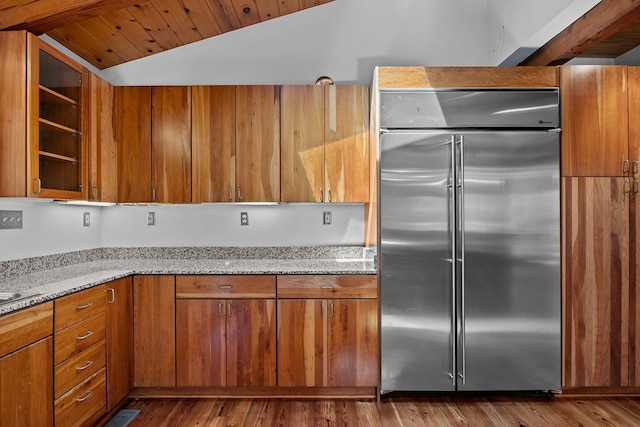 kitchen with built in refrigerator, wood ceiling, lofted ceiling, dark hardwood / wood-style floors, and light stone counters